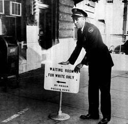 Police officer placing sign outside a rail station that says 'Waiting Room for White Only.' © 2012